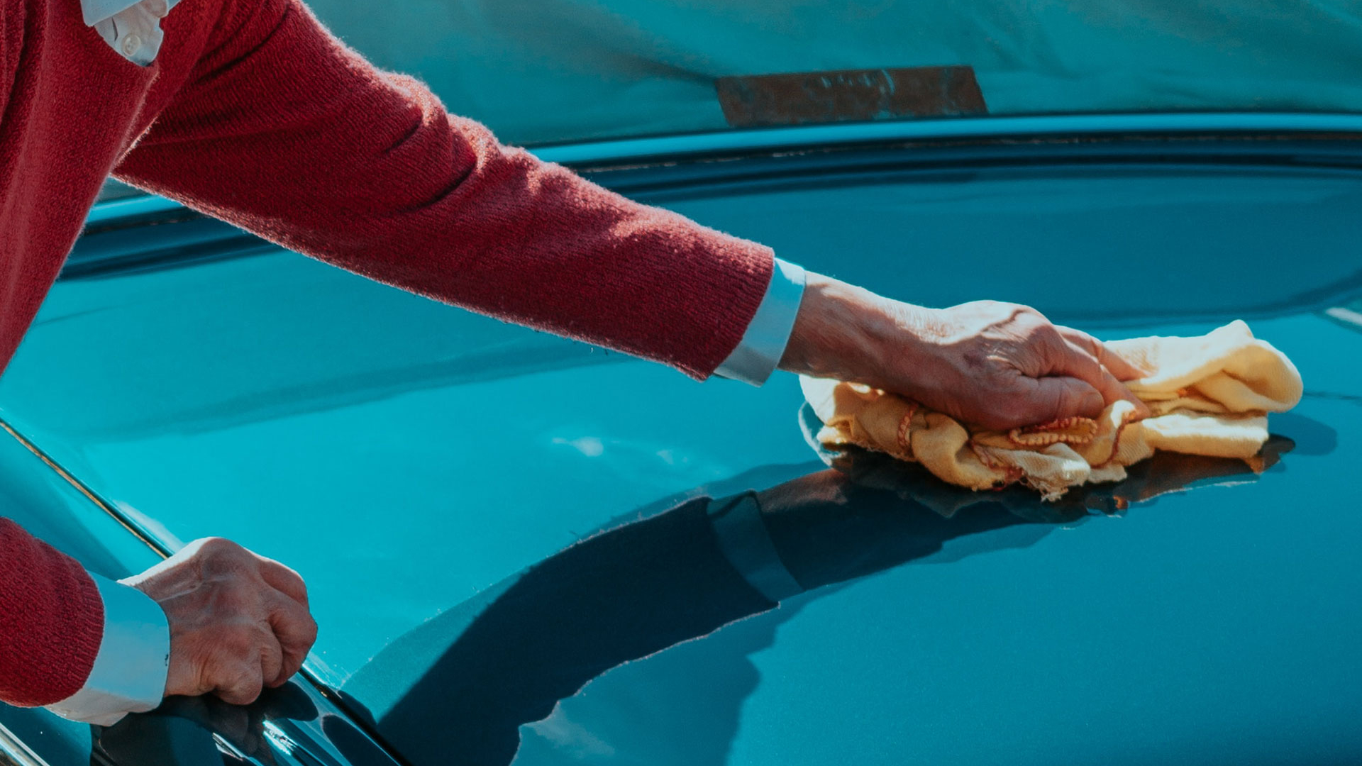 hand washing the front hood of a blue car